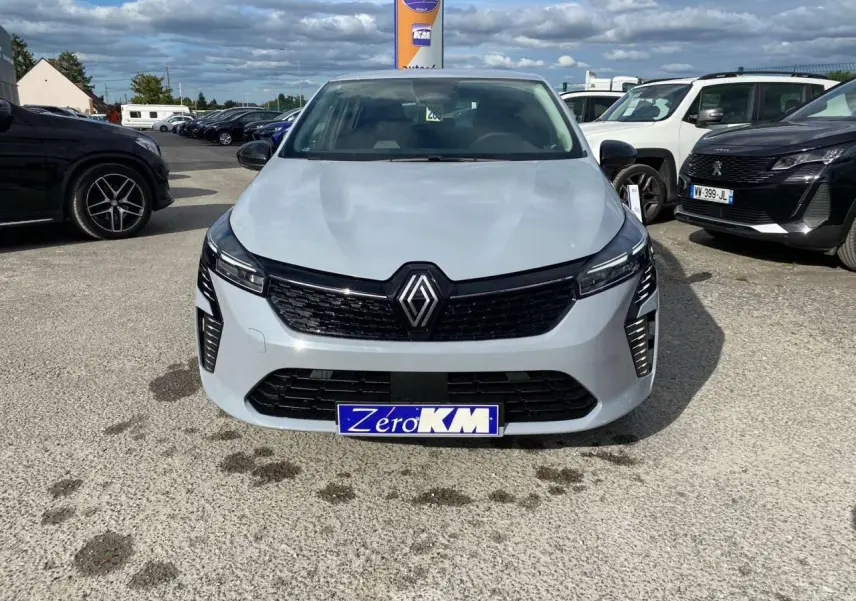 Vue frontale d'une Renault Clio 2025 gris Rafale avec calandre noire et phares LED allumés sur parking.