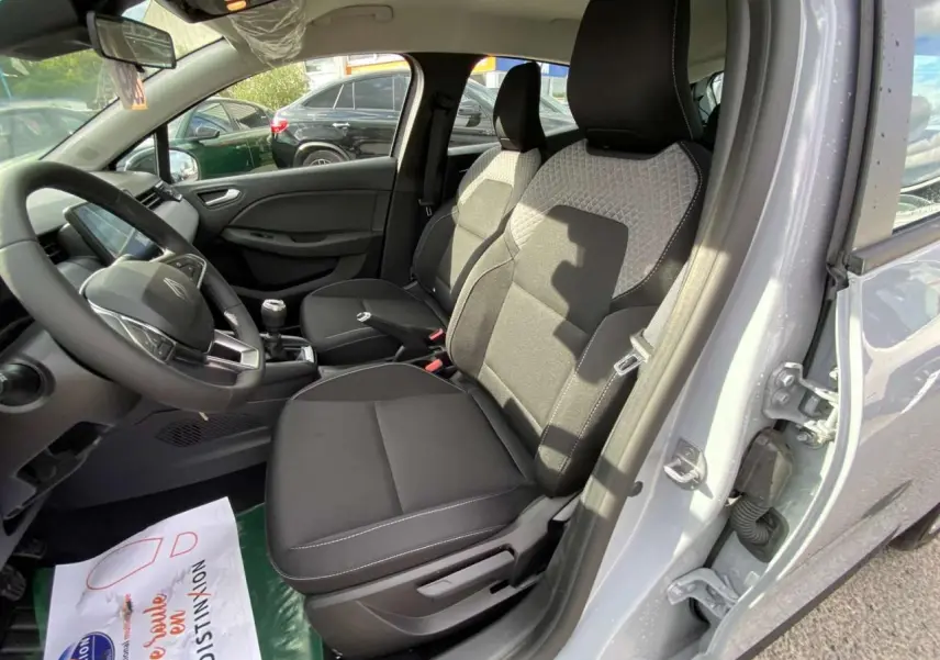 Intérieur de la Renault Clio 2025 gris Rafale, vue côté conducteur, sièges noirs avec surpiqûres blanches et volant multifonction.