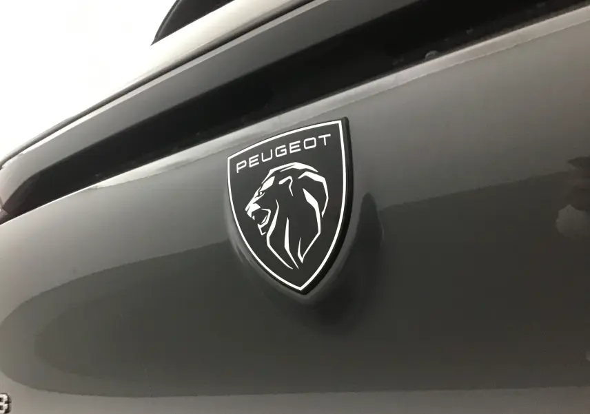 Gros plan sur l'écusson Peugeot noir et blanc sur la malle arrière gris Sellenium de la 308 2025.