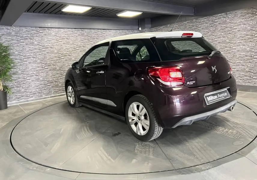 Vue 3/4 arrière droite d'une DS3 violet foncé avec toit blanc et canule d'échappement chromée en showroom.