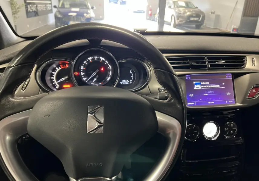 Vue intérieure du tableau de bord et volant cuir noir de la DS3 1.6 BlueHDi So Chic 2016 avec écran tactile allumé.