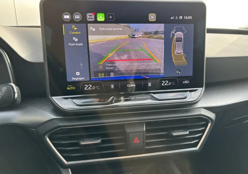 Vue rapprochée de l’écran central du SEAT Leon 2025 bleu Fjord affichant l’aide au stationnement avec caméra et réglages climatiques.