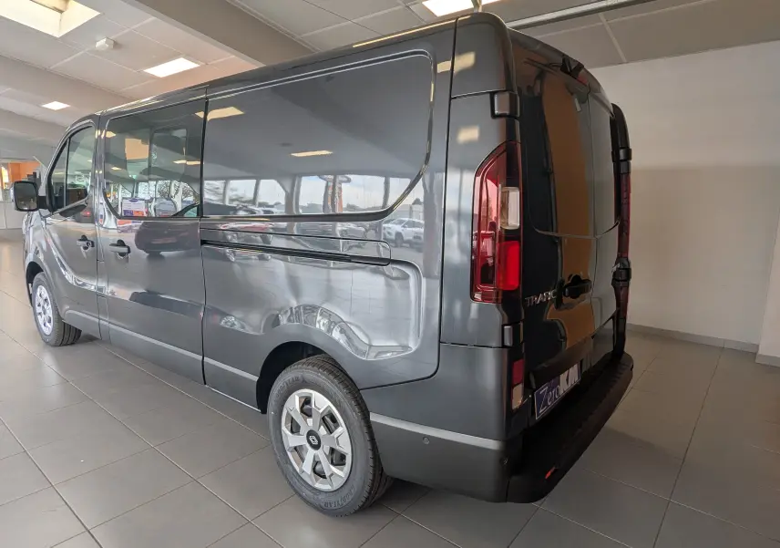 Renault Trafic Cabine Approfondie gris comète, vue 3/4 arrière droit en intérieur, avec jantes spécifiques et feux arrière visibles.