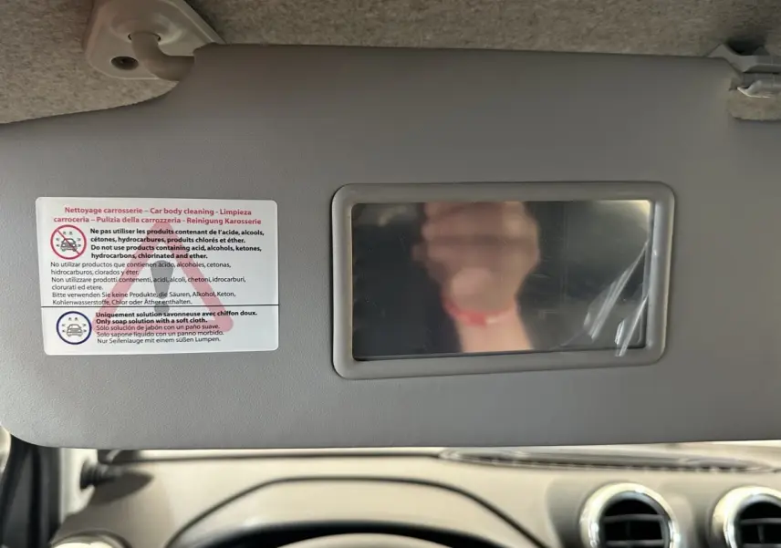 Vue intérieure centrée sur le pare-soleil avec miroir et consignes de nettoyage, tableau de bord beige visible en bas.