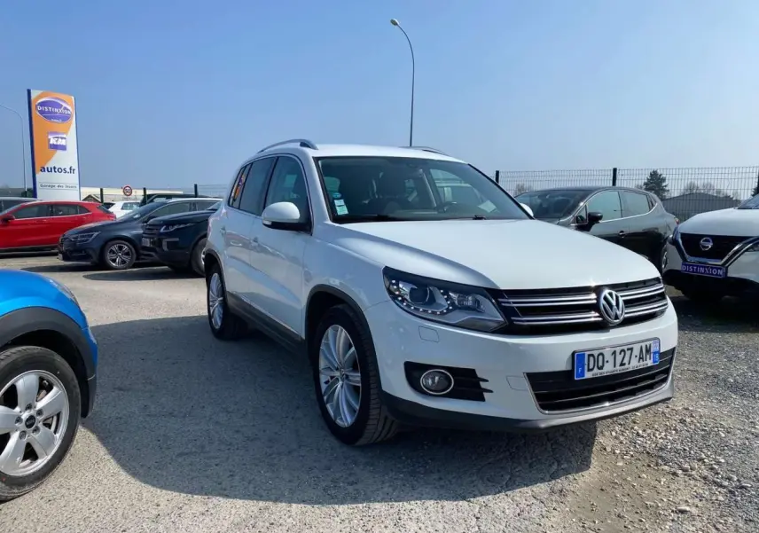 Volkswagen Tiguan blanc vu en 3/4 avant droit sur parking avec jantes alliage et calandre noire chromée.