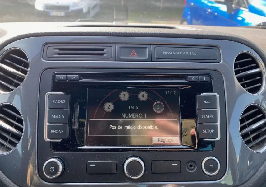 Gros plan sur l'écran multimédia central du Volkswagen Tiguan blanc de 2014 avec commandes radio et navigation visibles.