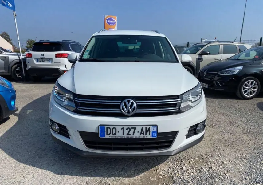 Volkswagen Tiguan blanc vu de face, avec calandre noire et feux avant allumés au soleil.