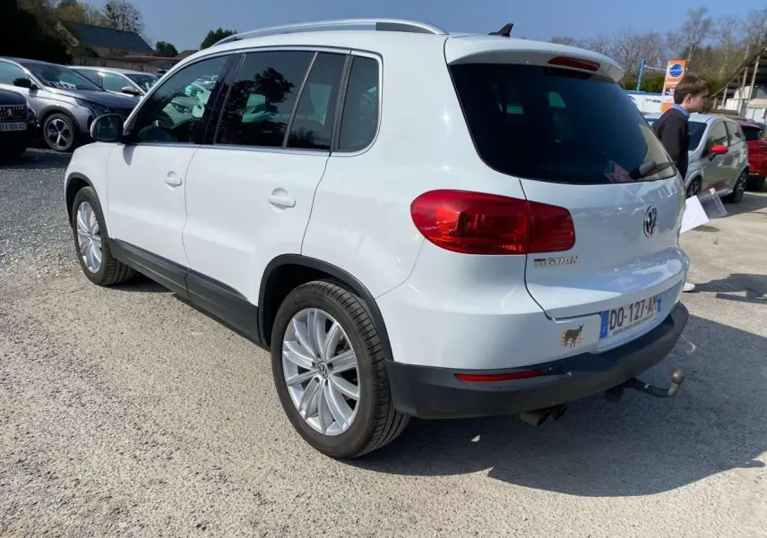 Vue 3/4 arrière droite d'un Volkswagen Tiguan blanc 2014 avec attelage et vitres arrière surteintées.