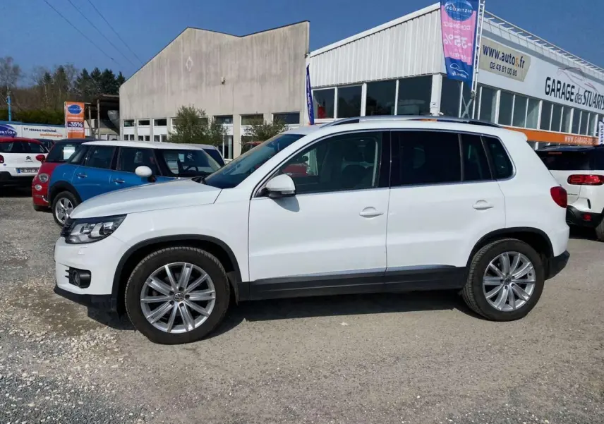 Volkswagen Tiguan blanc vu de profil côté gauche, avec jantes alliage 18 pouces et caméra de recul visible.