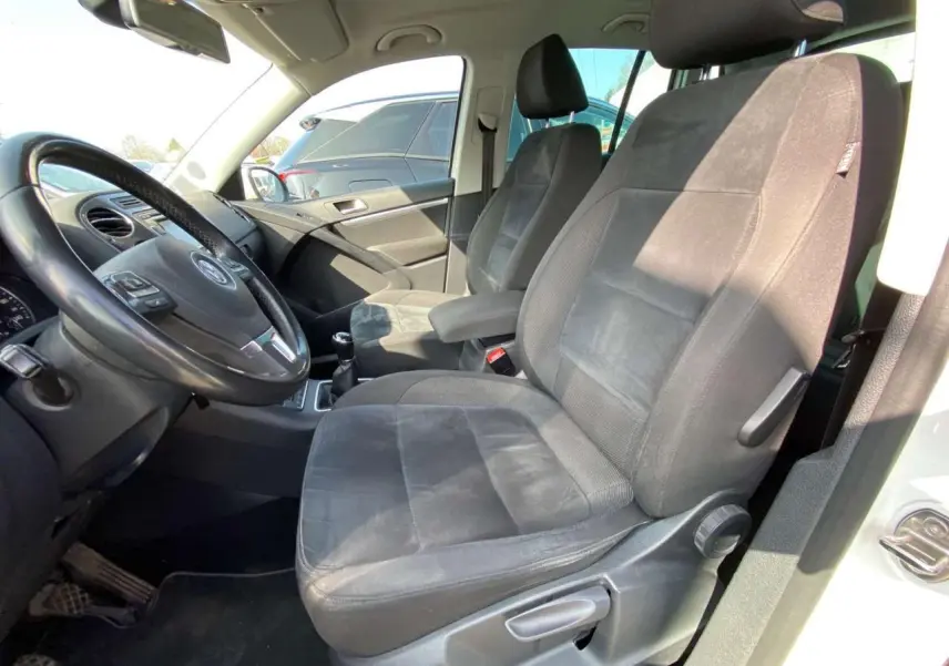 Intérieur avant droit du Volkswagen Tiguan blanc 2014, sièges tissu noir et volant cuir multifonction visible.
