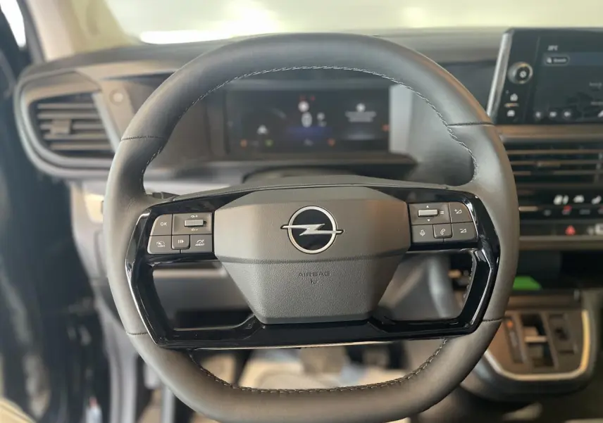 Gros plan sur le volant noir de l'Opel Vivaro 2025 avec commandes intégrées et tableau de bord numérique flou en arrière-plan.