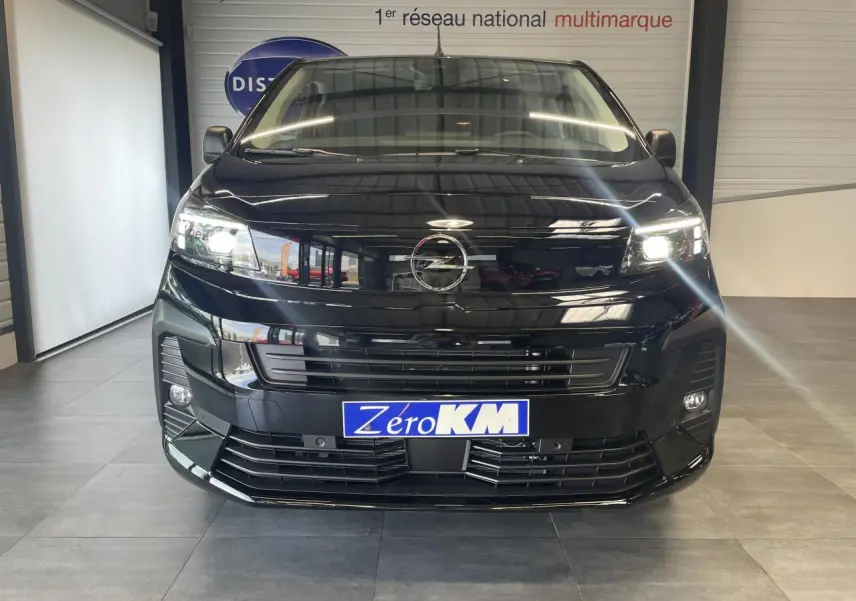 Vue frontale d'un Opel Vivaro noir carbone 2025 avec phares allumés et plaque Zéro KM visible.