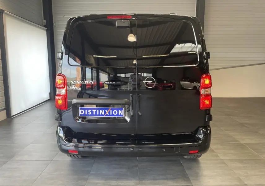 Vue arrière d'un Opel Vivaro noir carbone avec feux arrière allumés et plaque Distinxion dans un showroom.