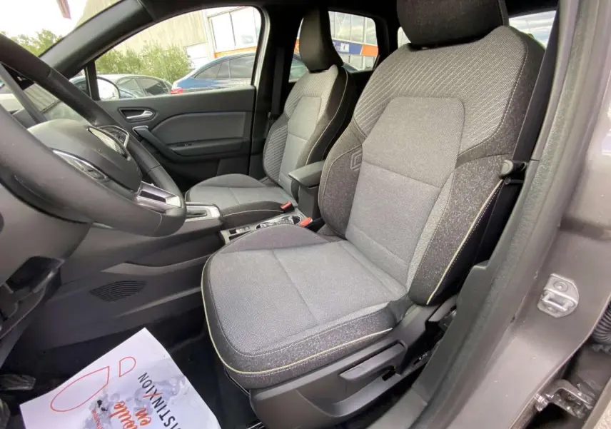 Vue intérieure côté conducteur du Renault Captur 2025, sièges tissu gris avec surpiqûres jaunes, volant et console visibles.