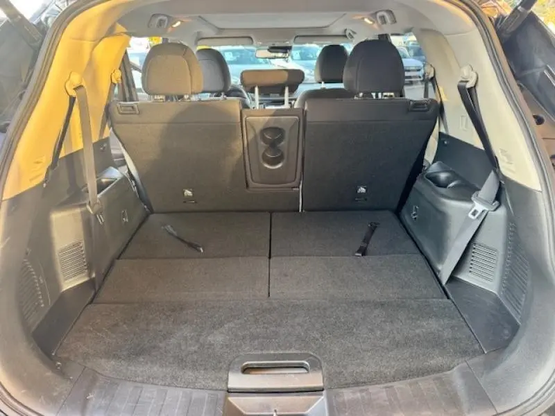 Vue arrière du coffre spacieux du Nissan X-TRAIL noir intense 2018 avec sièges arrière rabattus et accoudoir central visible.