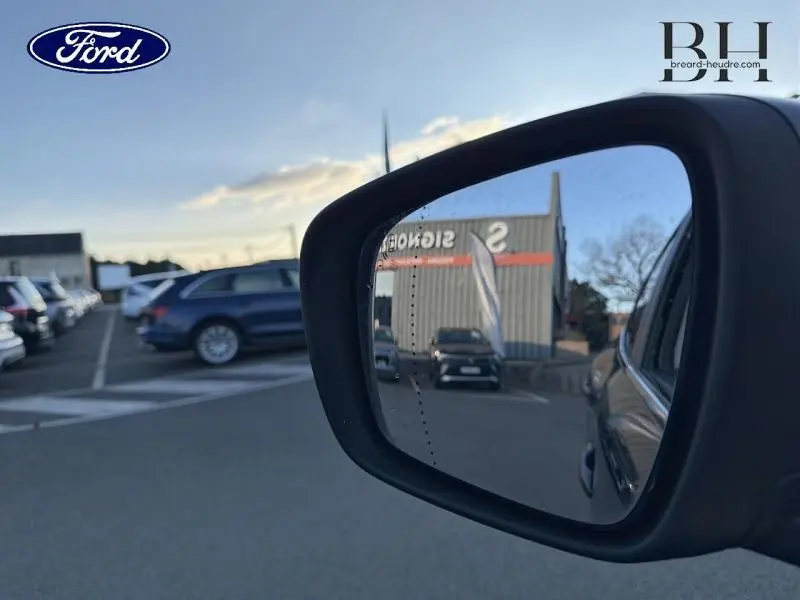 Rétroviseur extérieur droit d’un Renault Kadjar noir étoilé, reflet d’un parking et d’un bâtiment en arrière-plan.