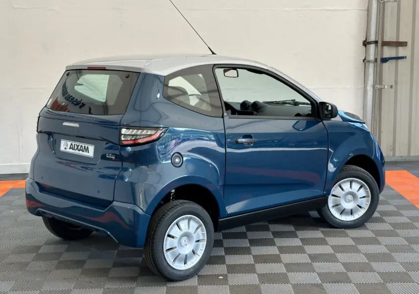 Vue 3/4 arrière droite de l'AIXAM Ambition 0.5 City Pack bleu avec toit blanc et caméra sur rétroviseur côté gauche.