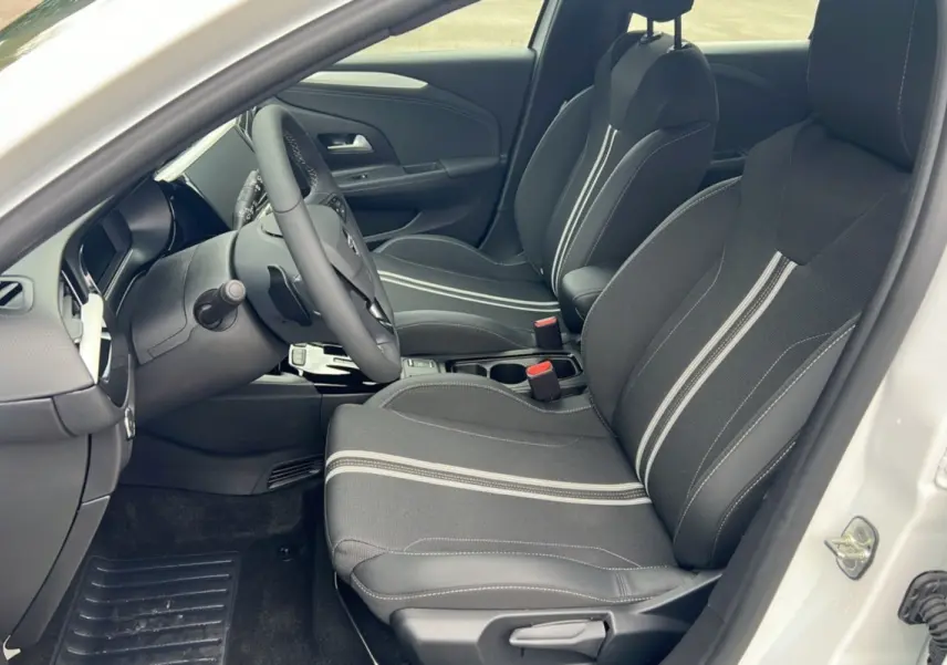 Vue intérieure côté conducteur d'une Opel Corsa blanc kontur 2026, sièges noirs avec surpiqûres claires et volant multifonctions cuir.