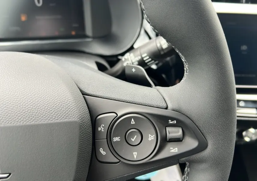 Gros plan sur les commandes multifonctions noires du volant cuir de l’Opel Corsa Hybrid blanc Kontur.