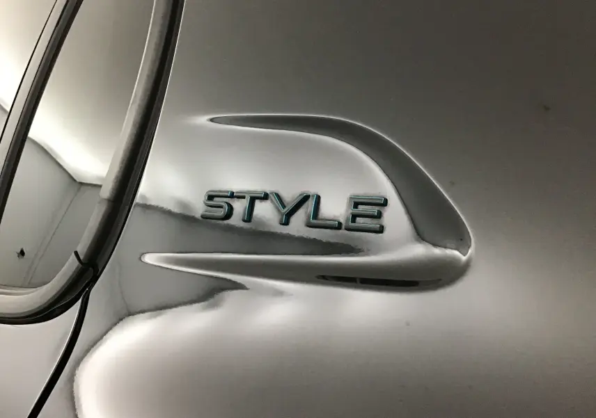 Gros plan sur l’inscription STYLE en relief sur la carrosserie noire brillante d’une Peugeot 208 1.2 PureTech 100 Style.