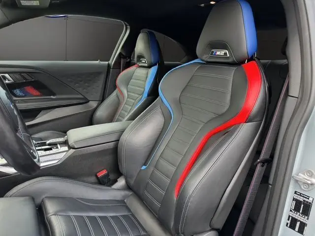 Intérieur BMW M2 G87 vue côté gauche sur sièges sport cuir noir avec surpiqûres bleues et rouges M2 brodées