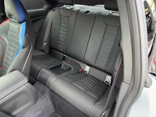 Vue intérieure arrière droite des sièges noirs en cuir de la BMW M2 G87 gris Brooklyn Grau avec surpiqûres rouges.