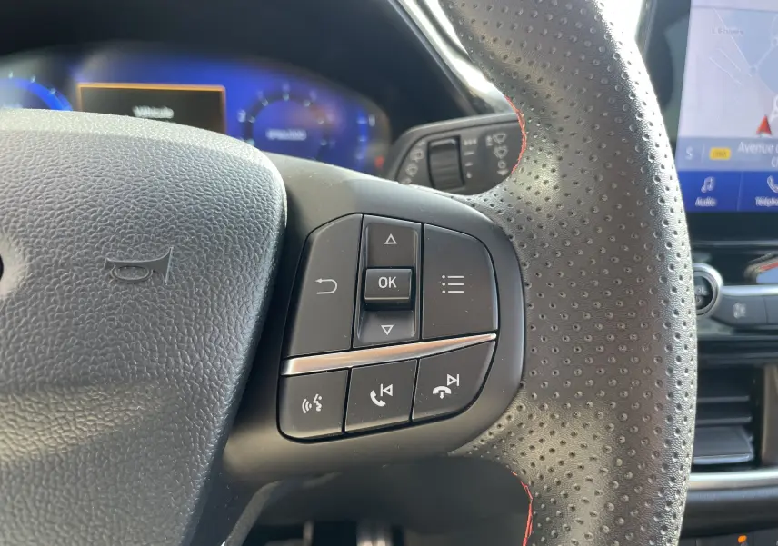 Gros plan sur les commandes multifonctions du volant perforé noir avec surpiqûres rouges du Ford Puma 2021.