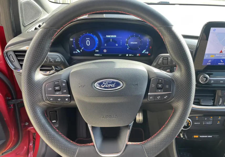 Vue rapprochée du volant perforé avec surpiqûres rouges et tableau de bord digital du Ford Puma rouge 2021.