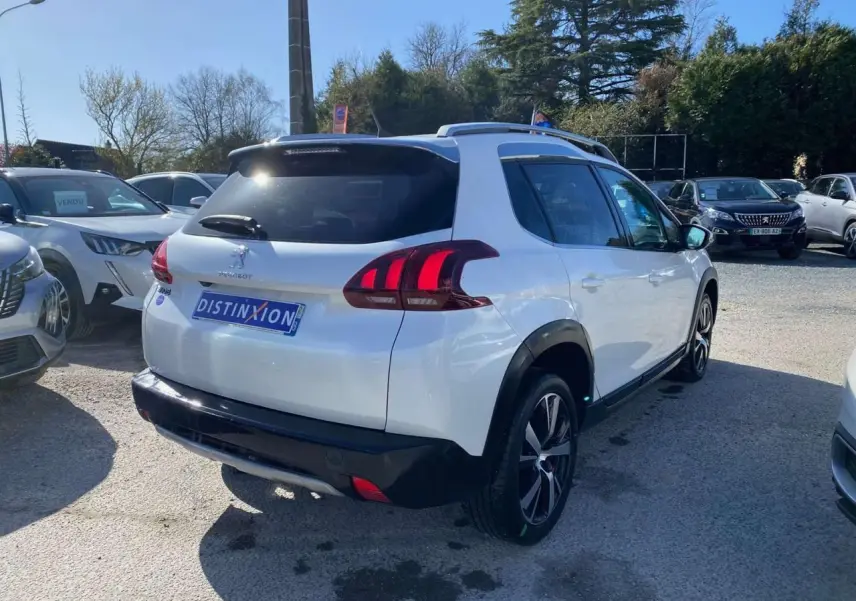 Vue 3/4 arrière droite d'un Peugeot 2008 blanc avec jantes aluminium 17'' et toit vitré panoramique en extérieur.