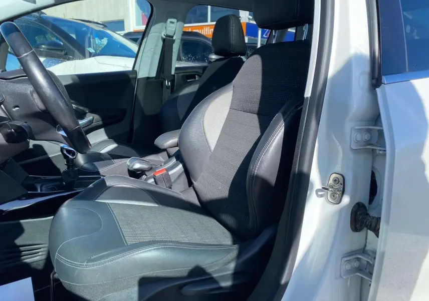 Vue intérieure côté conducteur d'une Peugeot 2008 blanche de 2019 avec siège en tissu et cuir noir.