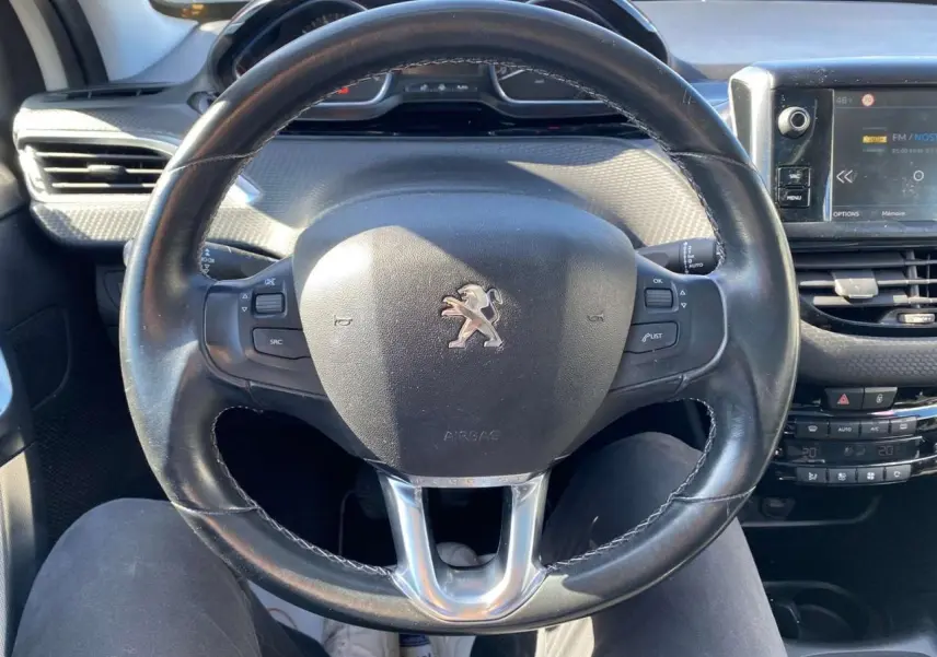 Vue rapprochée du volant cuir noir d'une Peugeot 2008 2019 avec tableau de bord et écran tactile multifonction.