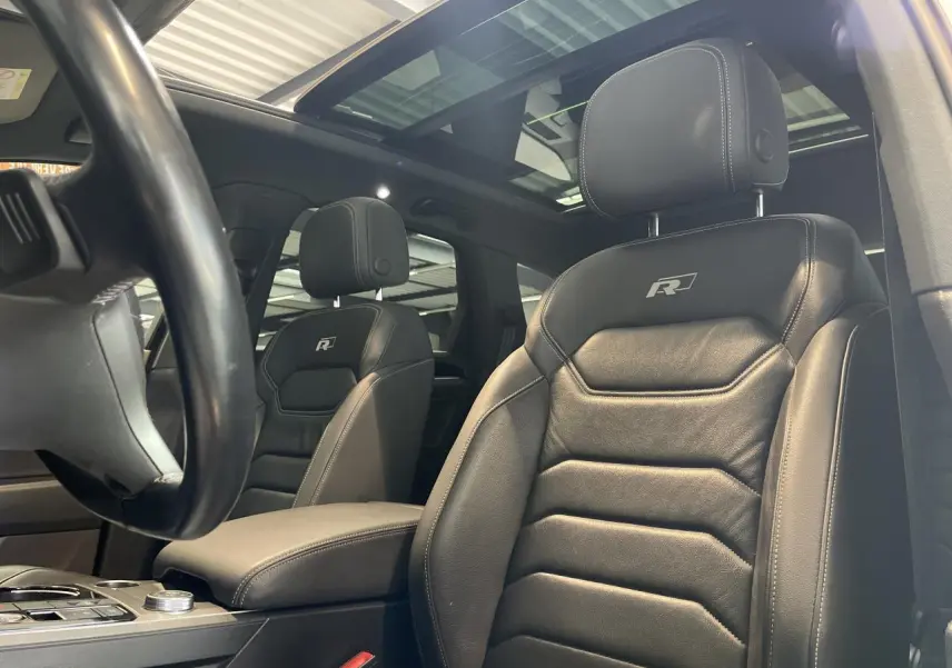 Vue intérieure rapprochée des sièges avant en cuir noir R-Line avec surpiqûres blanches et toit panoramique du Volkswagen Touareg blanc.
