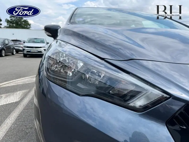 Gros plan sur le phare avant gauche d'une Nissan Micra gris acier, mettant en valeur la finition et les lignes du capot.