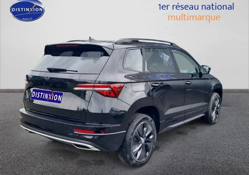Vue 3/4 arrière droite d'un Skoda Karoq noir 2025 avec jantes alu et barres de toit visibles.