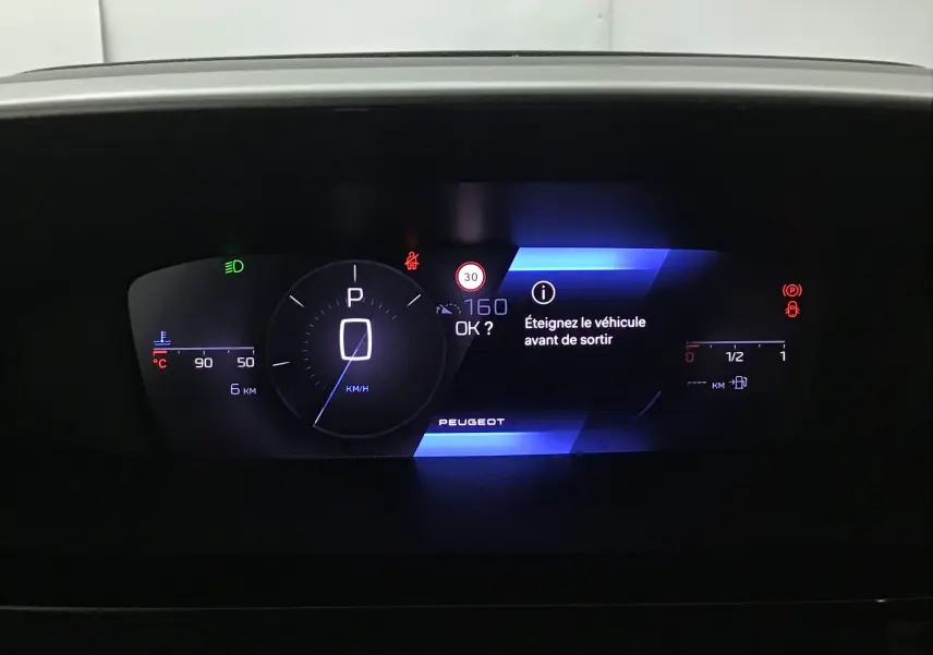 Tableau de bord numérique de Peugeot 308 2025 affichant vitesse, température moteur et message d'alerte.