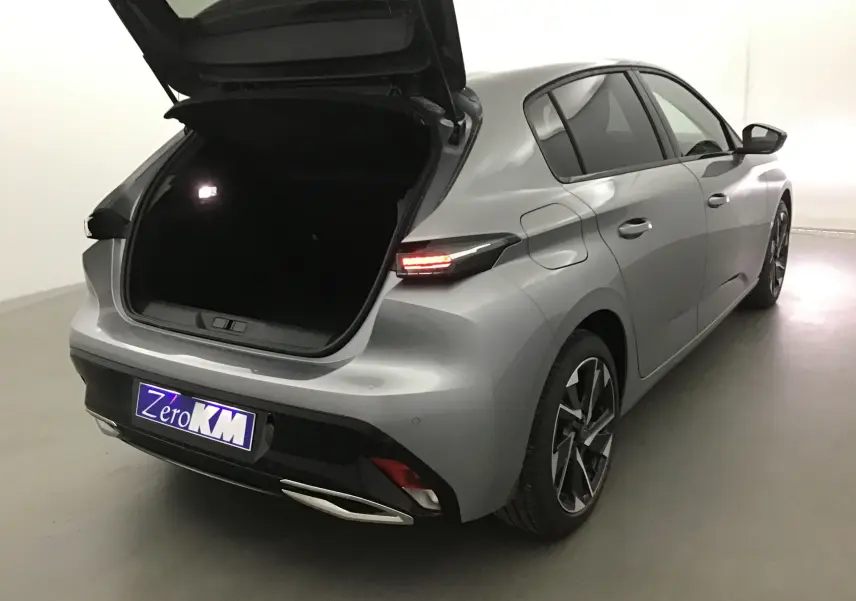PEUGEOT 308 gris Artense vue 3/4 arrière droit avec coffre ouvert et feux arrière allumés dans un studio lumineux.