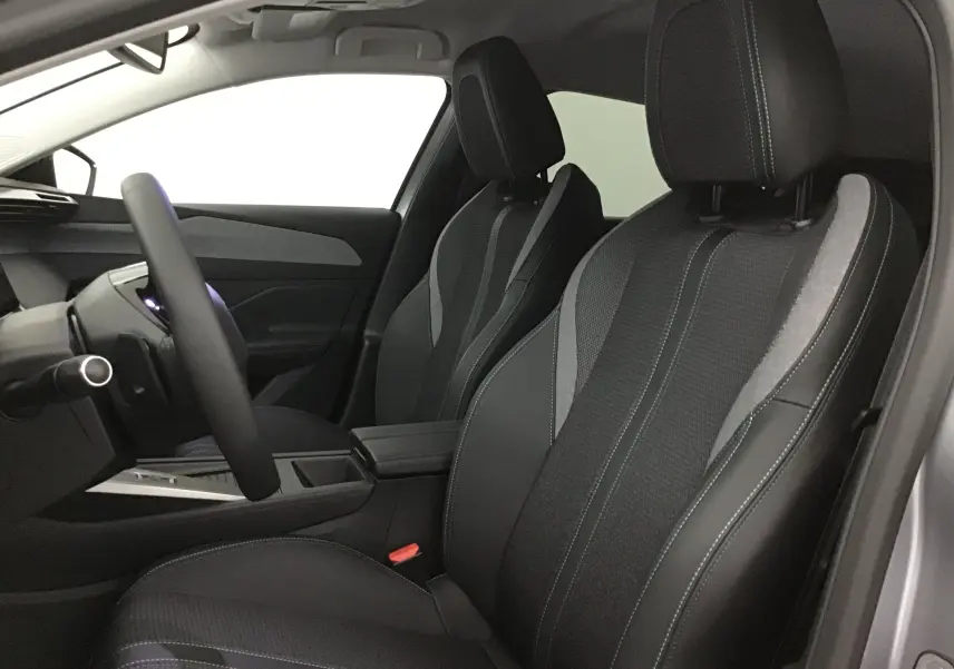 Vue intérieure côté conducteur de la Peugeot 308 2025 avec sièges en tissu noir et gris et volant multifonction.