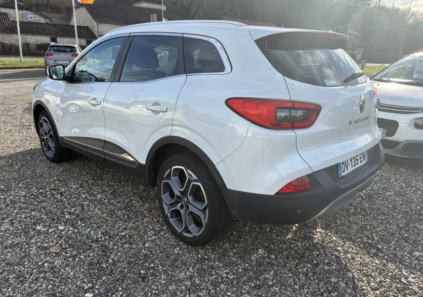 Renault Kadjar blanc vu en 3/4 arrière droit, avec jantes alliage et feux arrière distinctifs, stationné sur gravier.