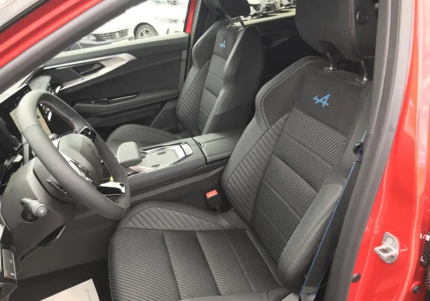 Vue intérieure côté conducteur du Renault Austral Esprit Alpine rouge et noir, mettant en valeur les sièges sport noirs avec surpiqûres bleues et logo Alpine brodé.