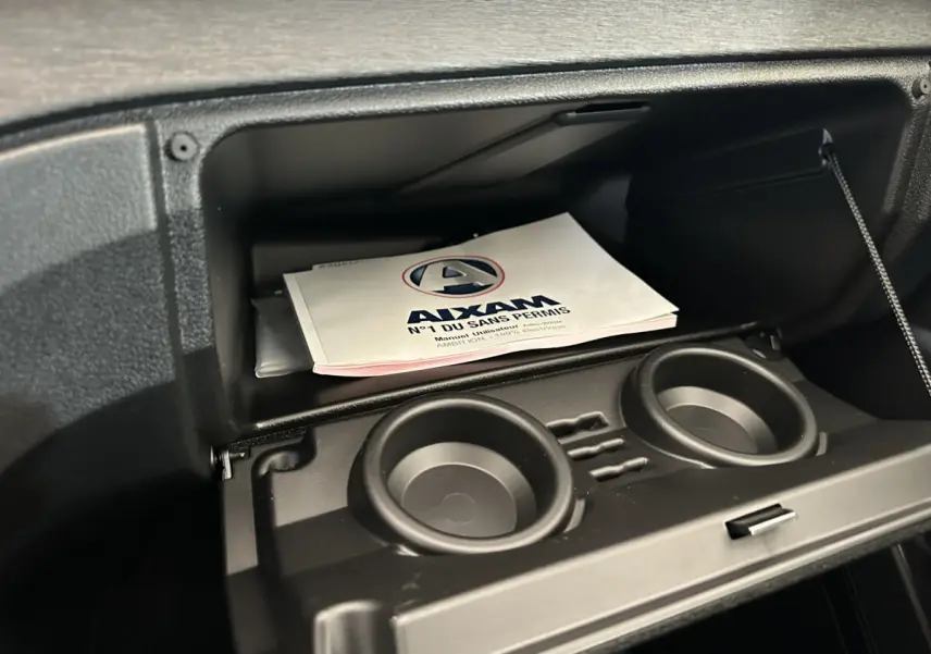 Gros plan sur la boîte à gants ouverte de l'AIXAM AMBITION E CITY PACK avec manuel utilisateur visible à l'intérieur.