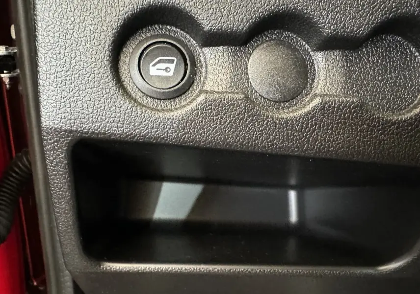 Bouton d'ouverture du coffre sur tableau de bord noir d'une Aixam Ambition E City Pack rouge, vue intérieure côté conducteur.