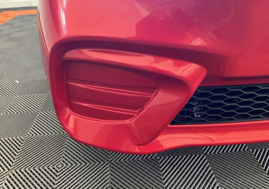 Gros plan sur le pare-chocs avant droit rouge de l'AIXAM AMBITION E CITY PACK 2026 avec grille noire ajourée.