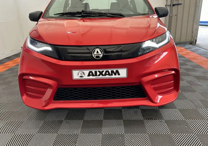 Vue frontale d'une Aixam Ambition E City Pack rouge 2026 avec calandre noire et phares LED allumés.