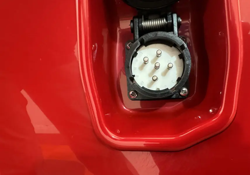 Gros plan sur la prise de recharge électrique intégrée dans la carrosserie rouge de l'AIXAM AMBITION E CITY PACK 2026.