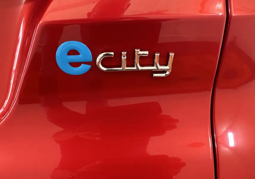 Gros plan sur l’inscription « e city » bleue et chrome sur la porte rouge vif de l’AIXAM AMBITION E CITY PACK 2026.