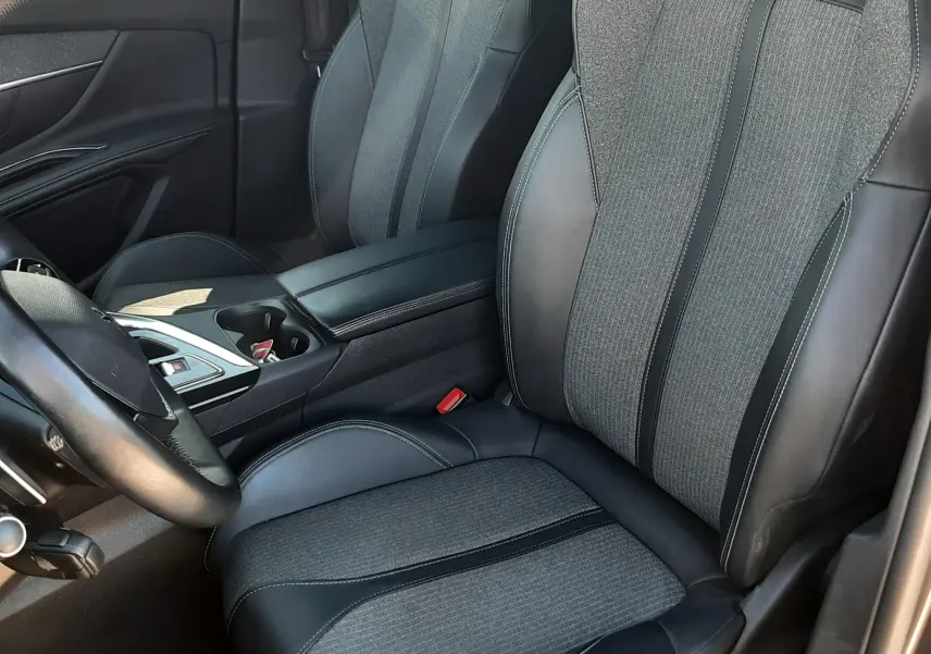 Vue intérieure côté conducteur du Peugeot 3008 2023, sièges tissu gris et cuir noir avec coutures contrastées.