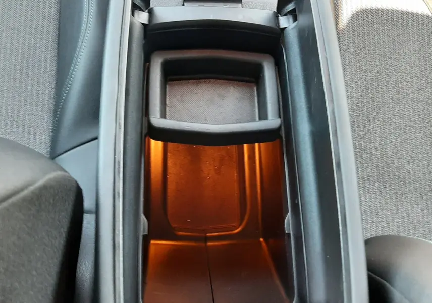 Vue plongeante sur le rangement central éclairé en orange du Peugeot 3008 2023, avec porte-gobelets et sièges tissu gris.