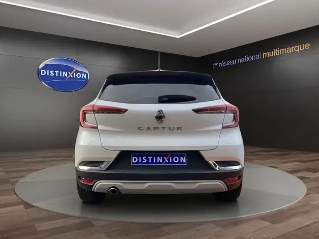 Vue arrière d'un Renault Captur blanc nacré avec toit noir, stationné en intérieur sur un plateau rotatif showroom.
