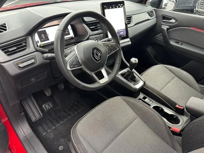 Vue intérieure côté conducteur du Renault Captur 2025, volant multifonction, boîte manuelle et sellerie grise avec surpiqûres rouges.