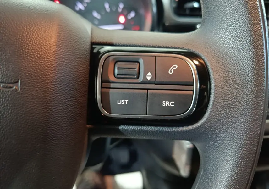Gros plan sur les commandes gauche du volant noir de la Citroën C3 2024, boutons LIST, SRC et téléphone visibles.